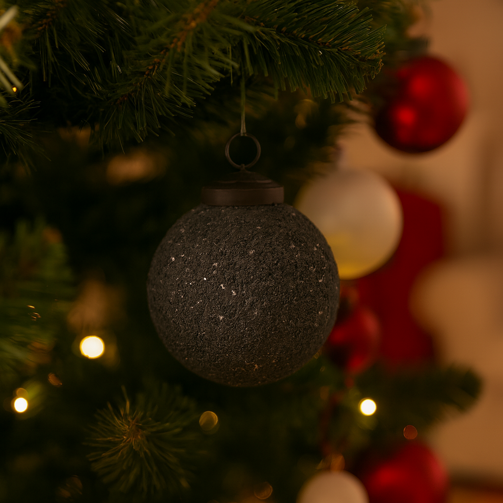 Mørk grå julekule med grov tekstur henger på juletre med røde og hvite kuler og varmhvite lys.
