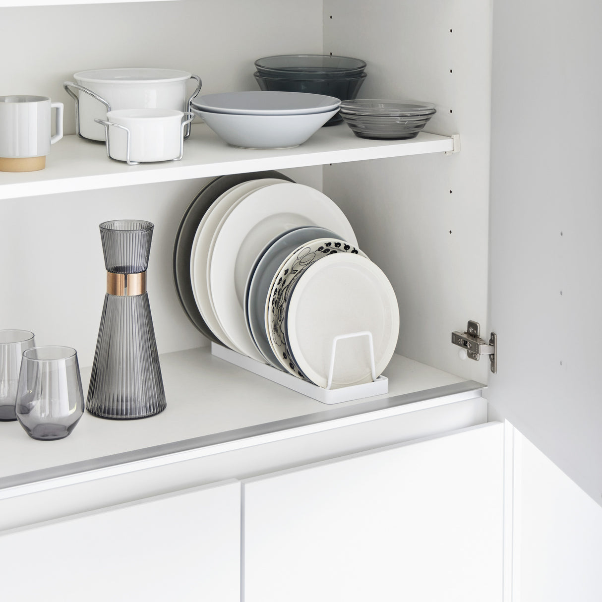 Hvitt tallerkenstativ med oppreist lagring, plassert i skap med servise.
