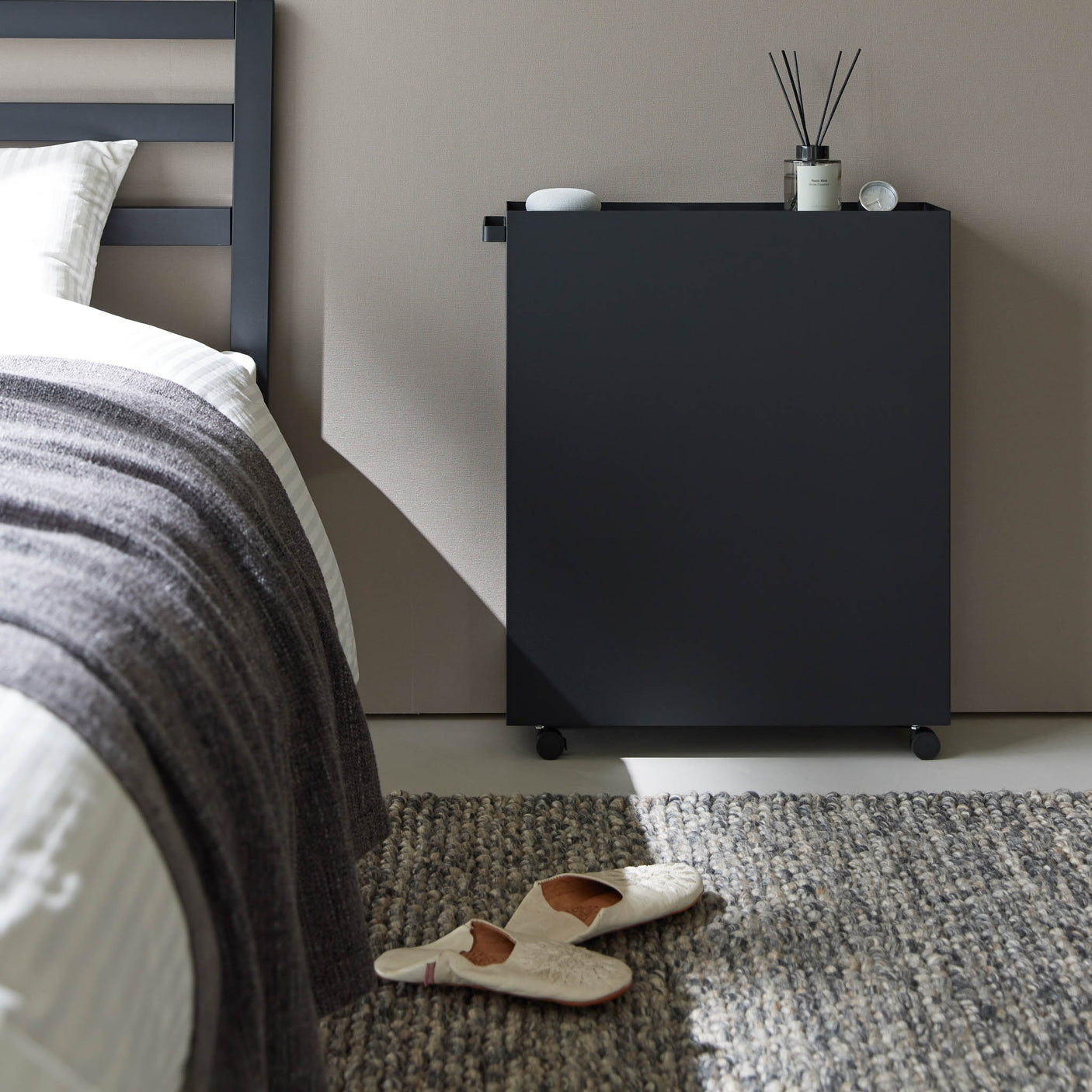 Sort oppbevaringsvogn med tre hyller plassert ved siden av skrivebord.