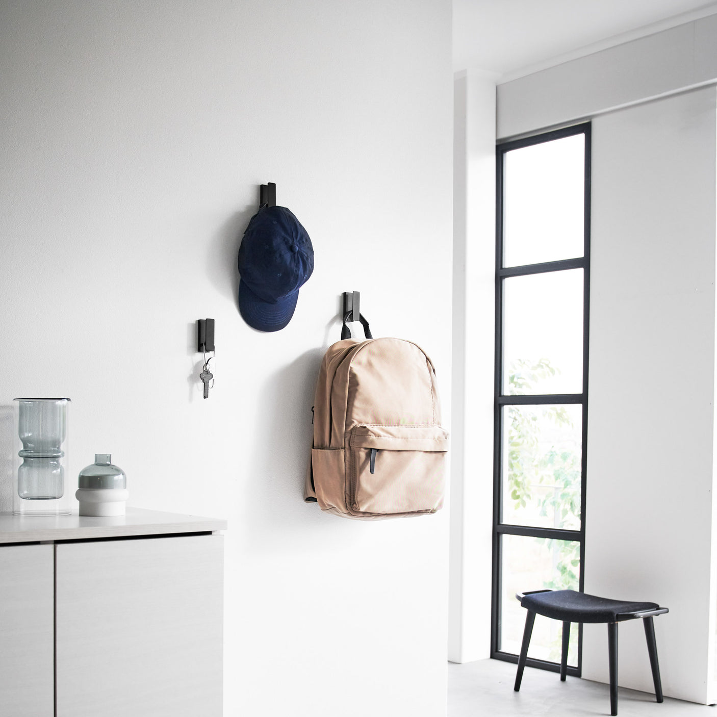 3pk sorte kroker i metall festet på rekke i gang med klær hengende.