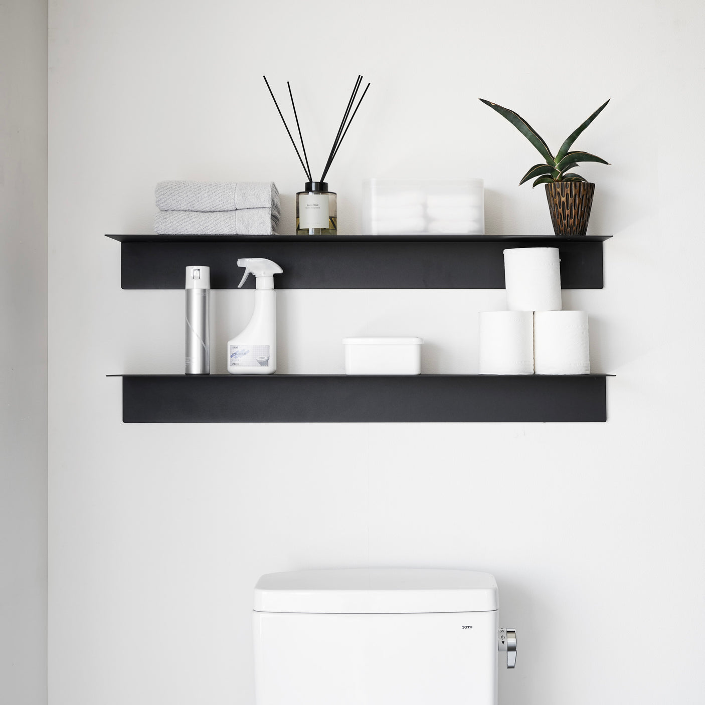 To sorte veggmonterte hyller over toalett med dekor og planter