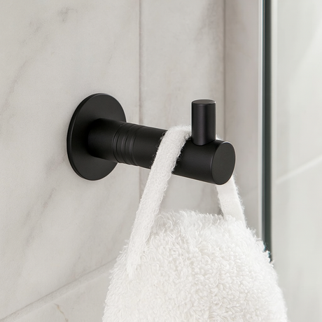 Moderne sort håndkleknagg i metall montert på vegg med hvitt frottéhåndkle, perfekt for stilfullt bad eller kjøkken