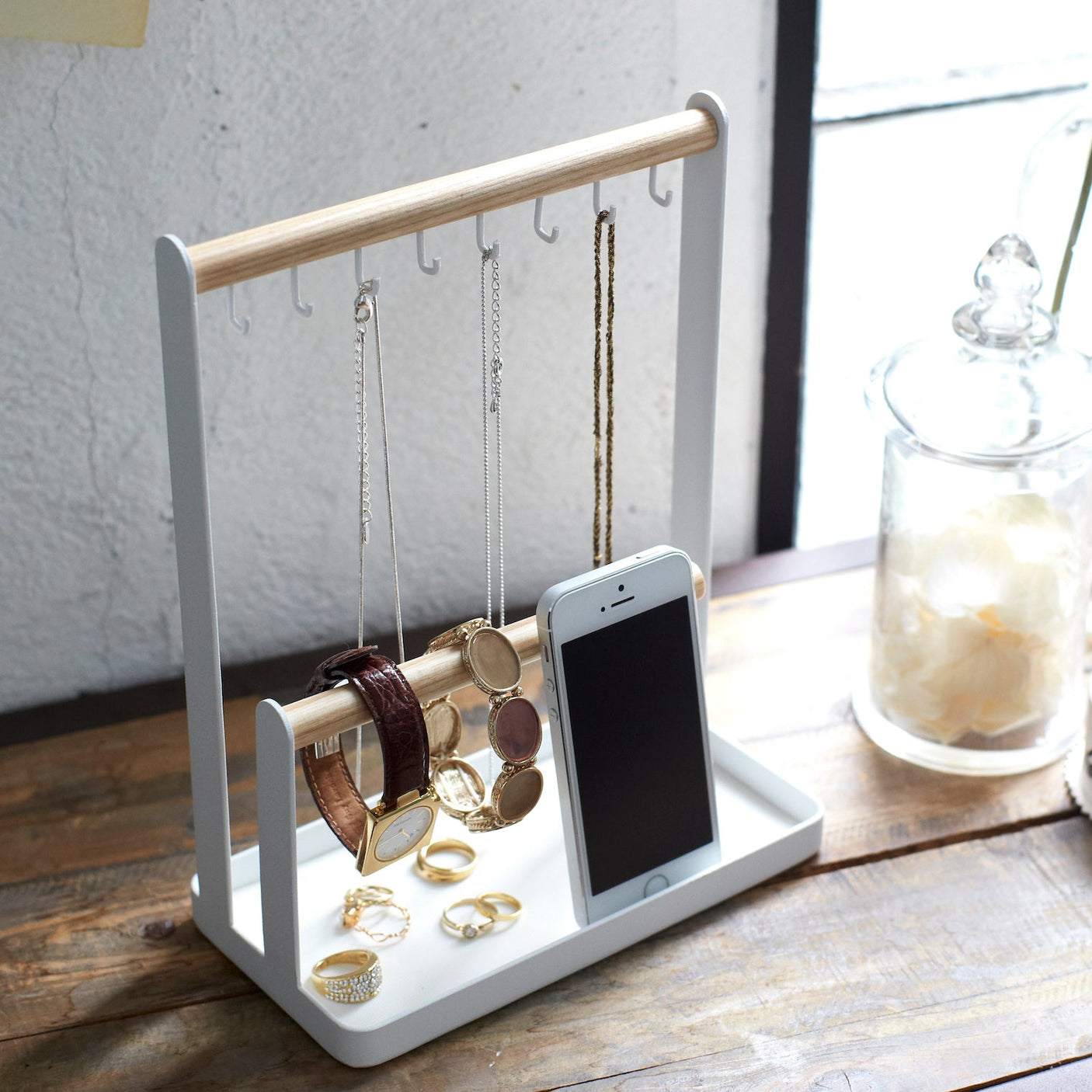 Smykkestativ med metallramme og trestenger, plassert på et bord med smykker.