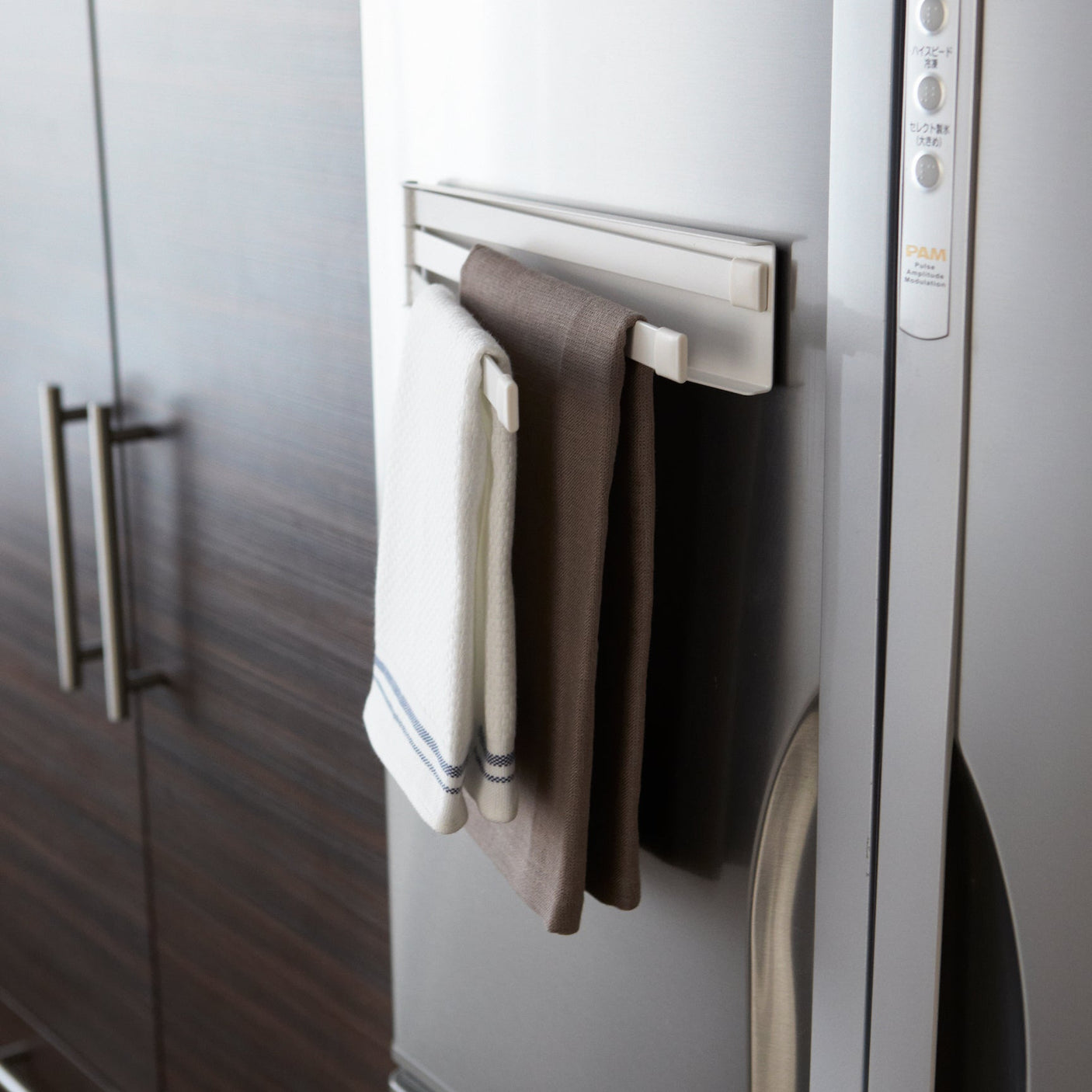 Hvit magnetisk håndkleholder festet til et kjøleskap med to kjøkkenhåndklær hengende.