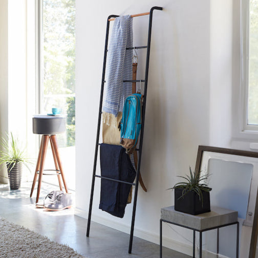 Sort stigehenger lent mot en vegg, med klær og tilbehør hengende på trinnene.