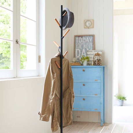 Sort stumtjener med treknagger, plassert i en lys entré med en jakke og hatt hengende.