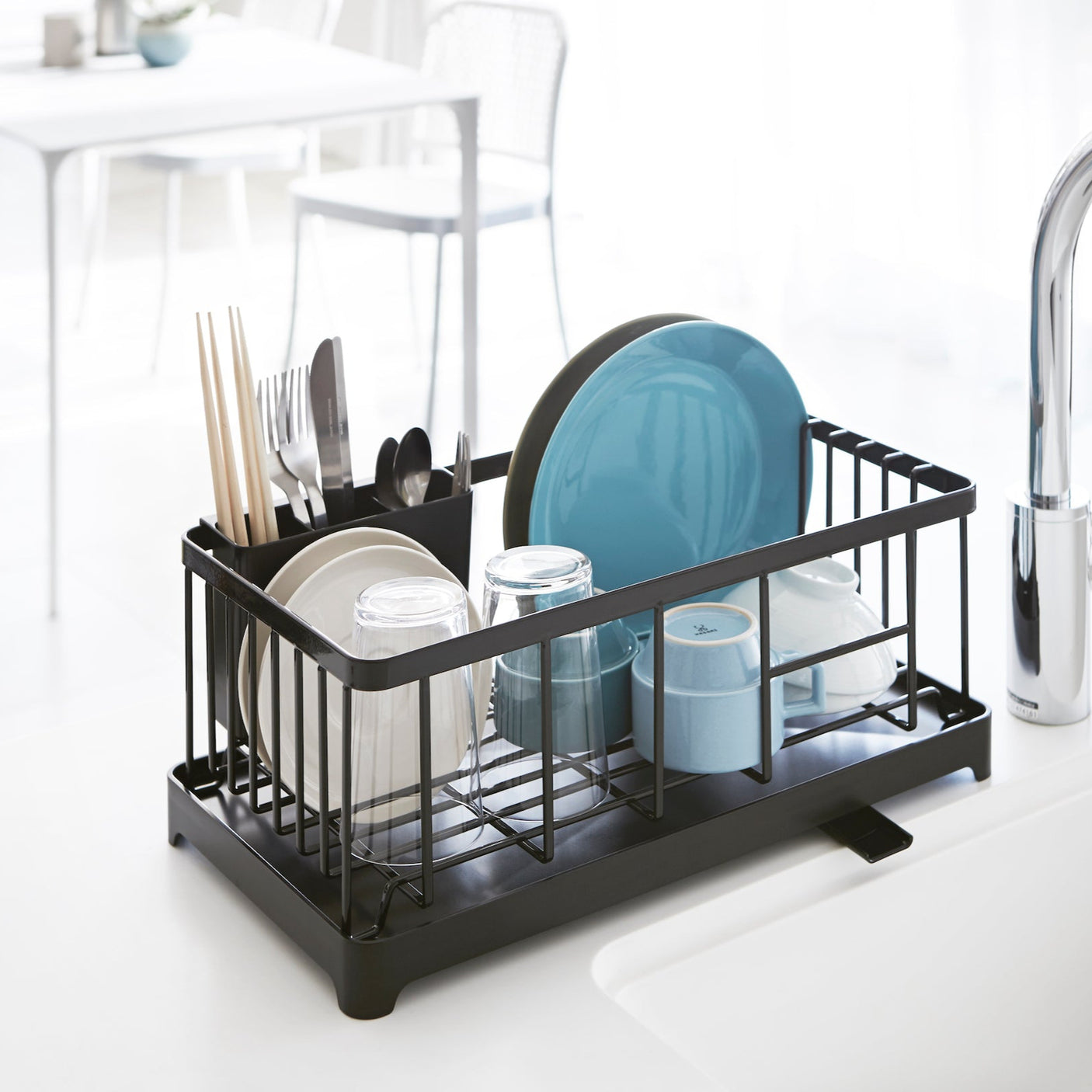 Sort oppvaskstativ med drypprenne plassert ved vasken, fylt med tallerkener og glass.