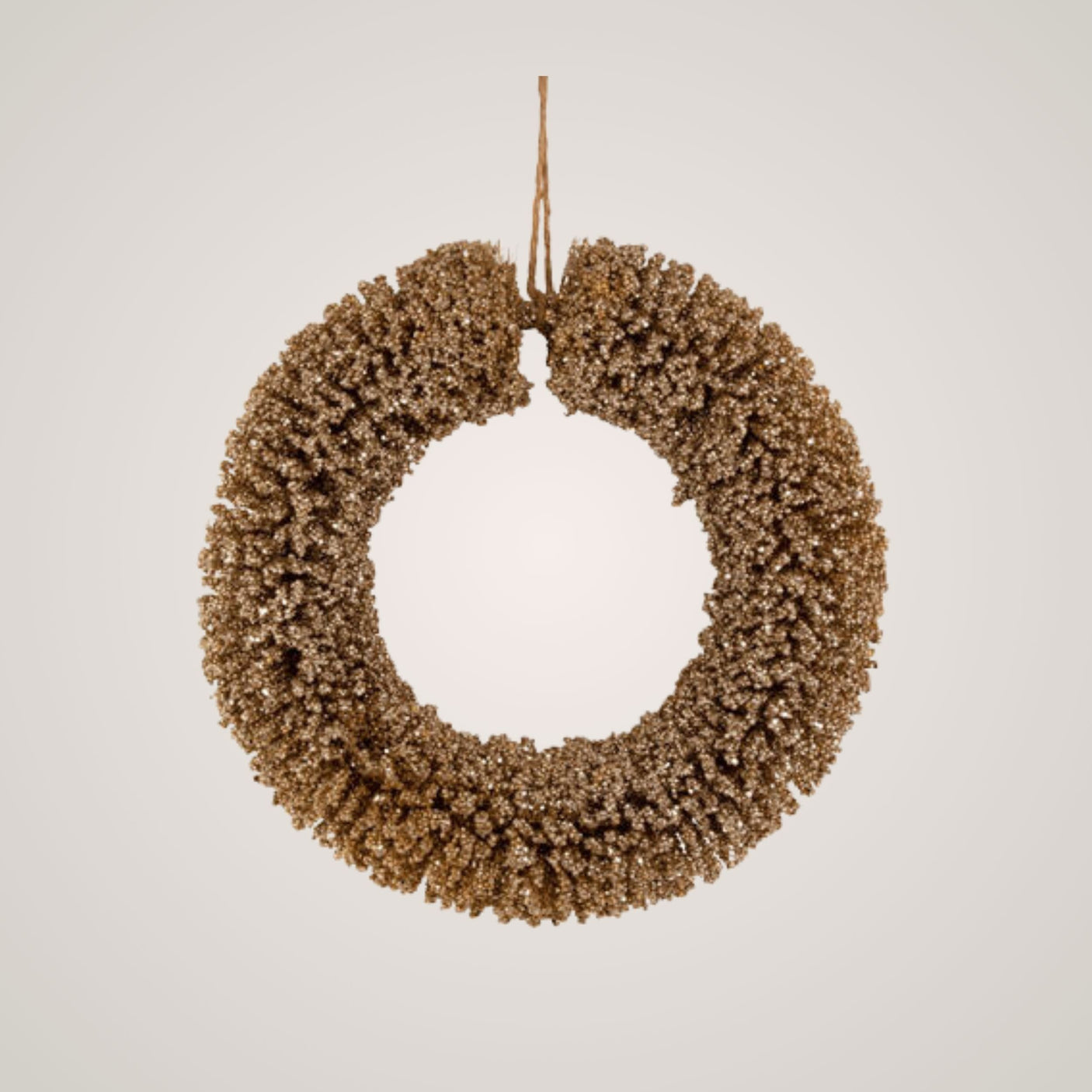 Gullglitrende julekrans hengt opp med brun snor mot lys bakgrunn, sett rett forfra.