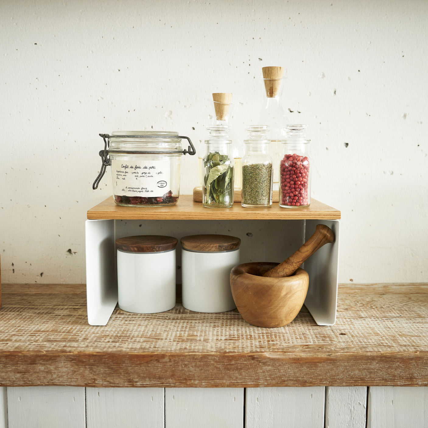 Oppbevaringshylle i hvit metall med treplate på kjøkkenbenk.
