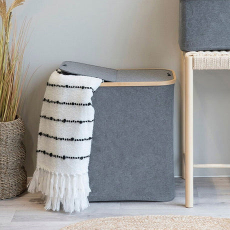 Grå skittentøyskurv med lokk og bambusramme plassert på badet med teppe og pledd.