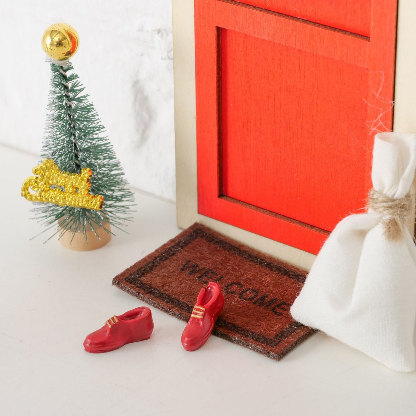 Miniatyrsett montert foran vegg med rød dør, stige, lykt og julepynt.