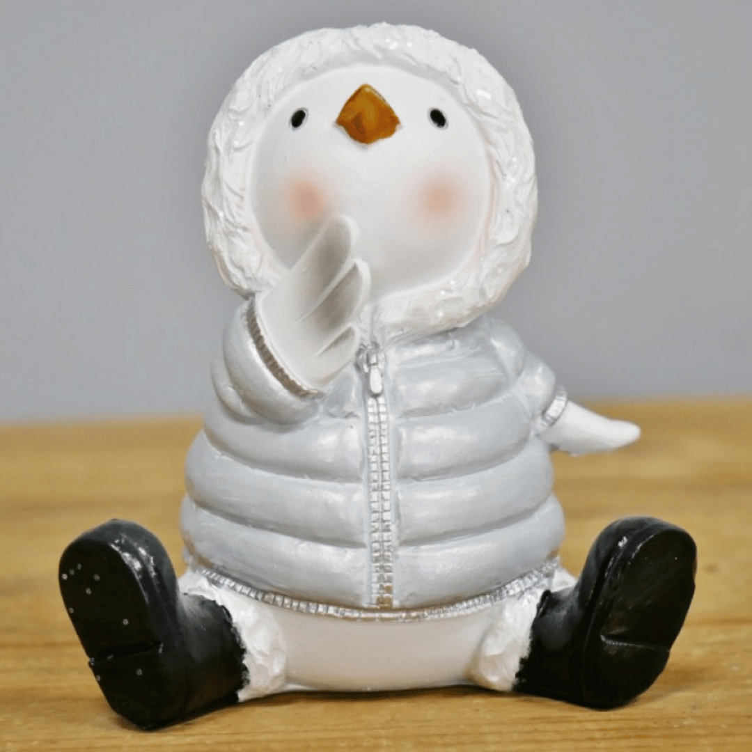 Sittende julefugl i hvit vinterjakke med hette og svarte støvler.