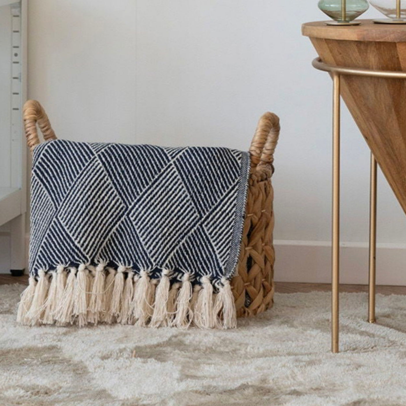 House Nordic Izmir pledd i kurv med dusker og mønster – dekorativ detalj i moderne stue med stol, sidebord og lyse, nordiske fargetoner.