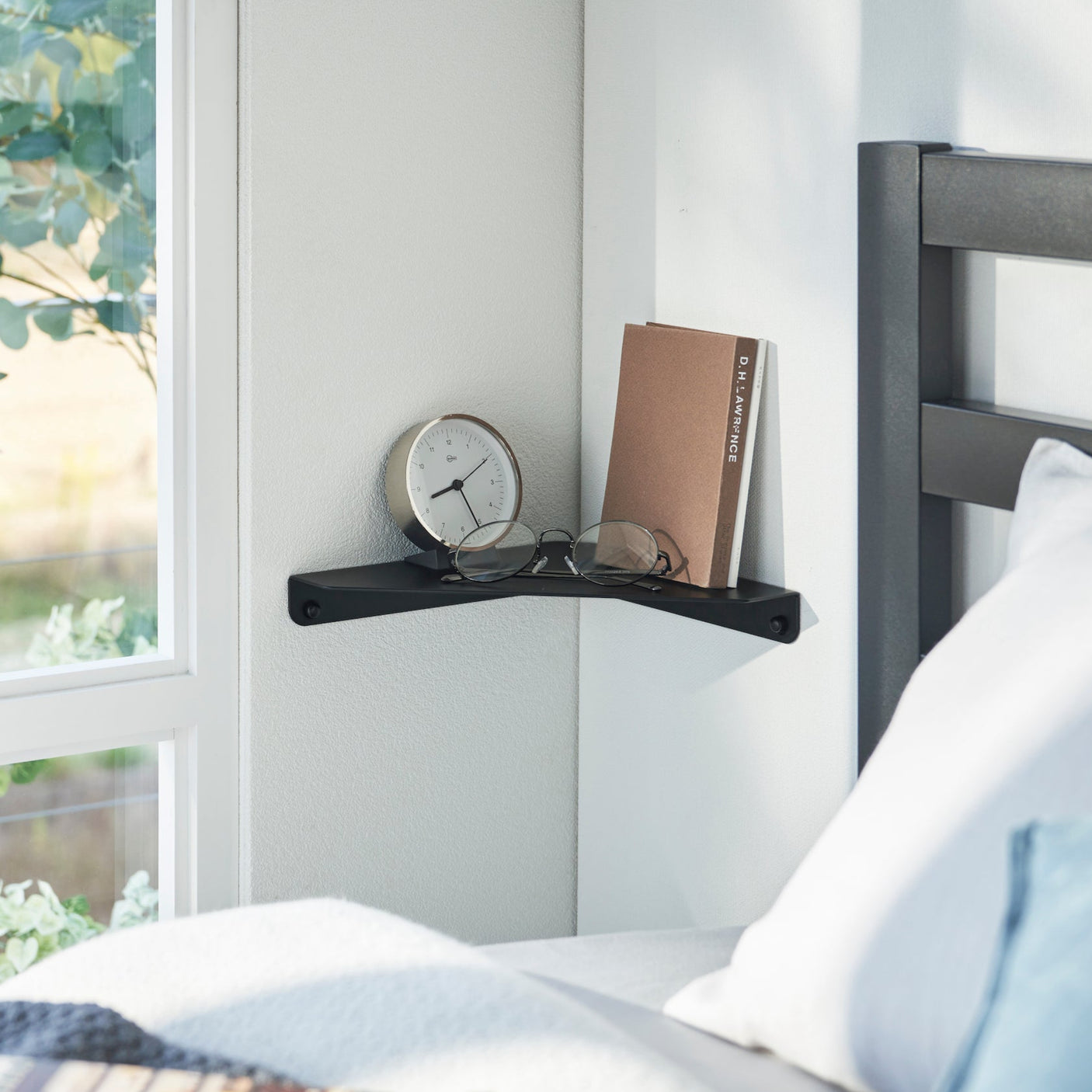 Sort hjørnehylle montert på veggen ved sengen.