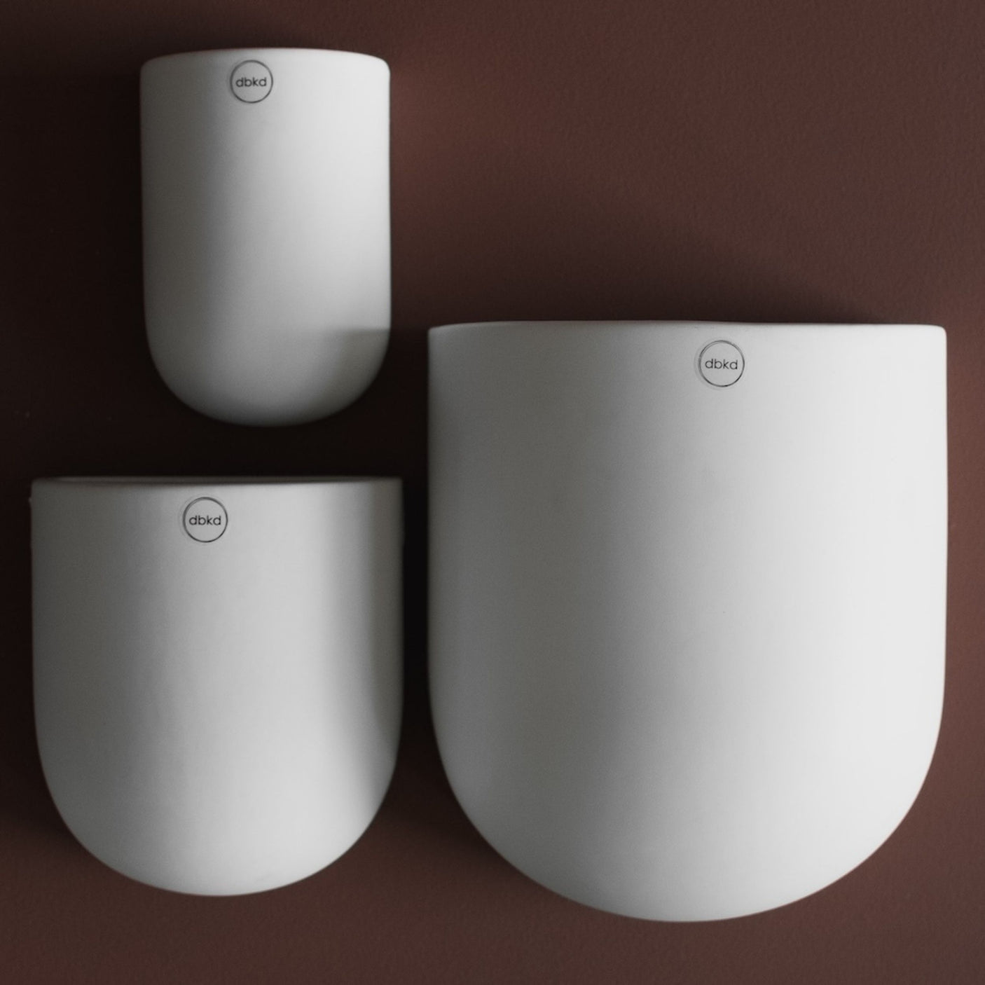 Stor keramikkpotte for vegg i nøytral farge og avrundet form.