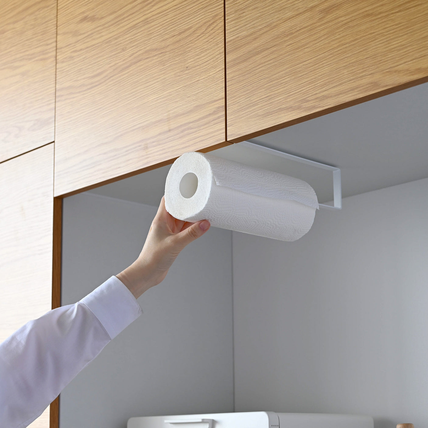 Person monterer kjøkkenpapir på stativ under skap