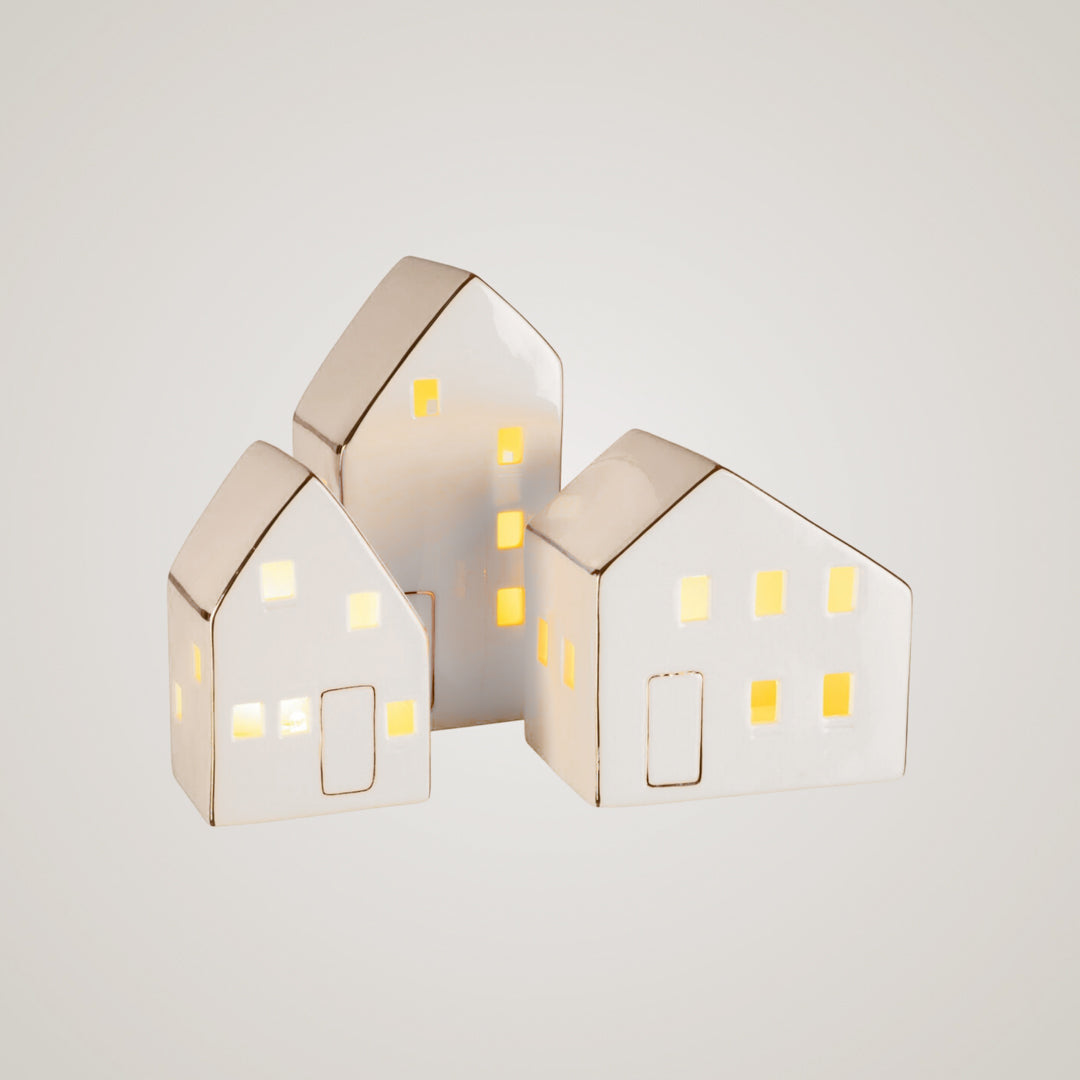 Tre keramikkhus med varme lys i vinduene, plassert sammen på lys bakgrunn.