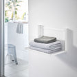 Hvit sammenleggbar vegghylle montert på bad med håndklær.