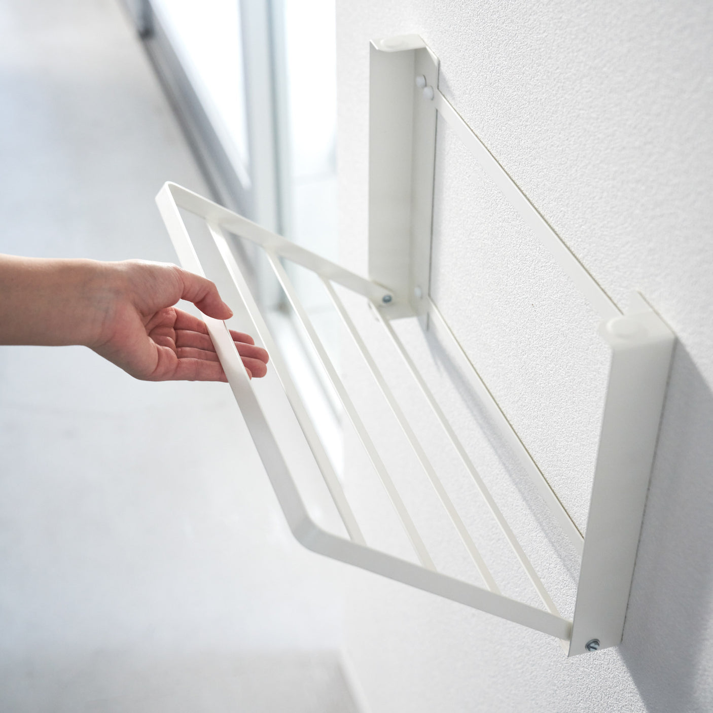 Praktisk sammenleggbar hylle i hvit metall montert ved dusj.