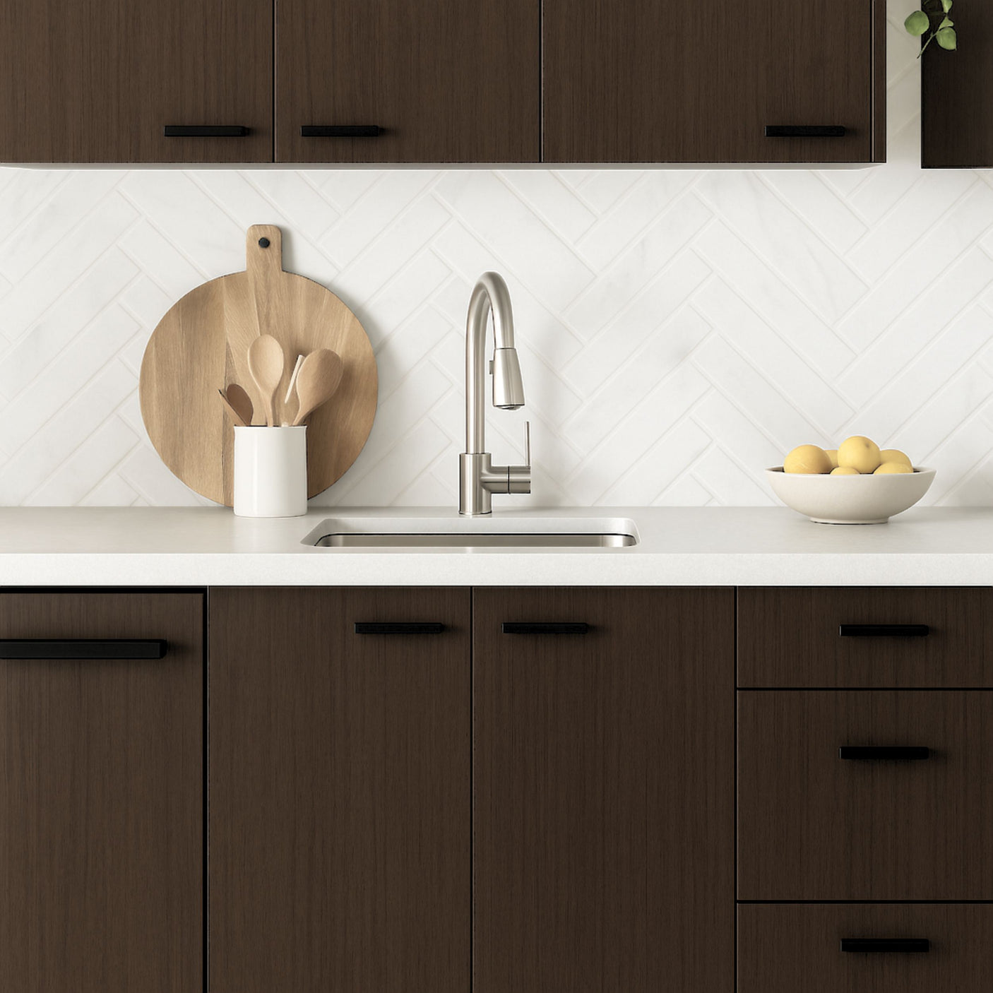 Kjøkken med Cocoa kontaktplast på skap, hvit benkeplate, fiskebensmønstret flis og innslag av tre og sitroner som dekor.