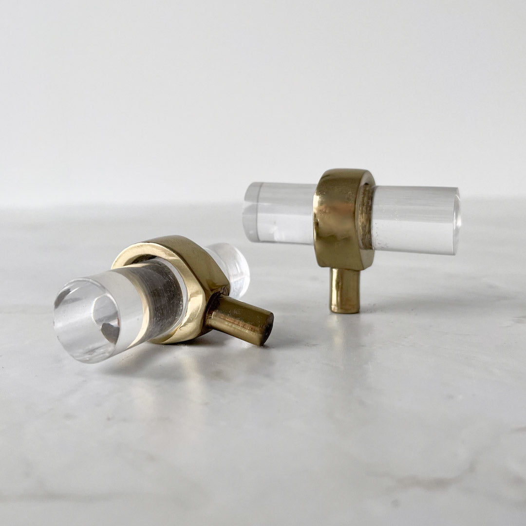 To Nesu T-bar knotter i glass og messing liggende på lys overflate.