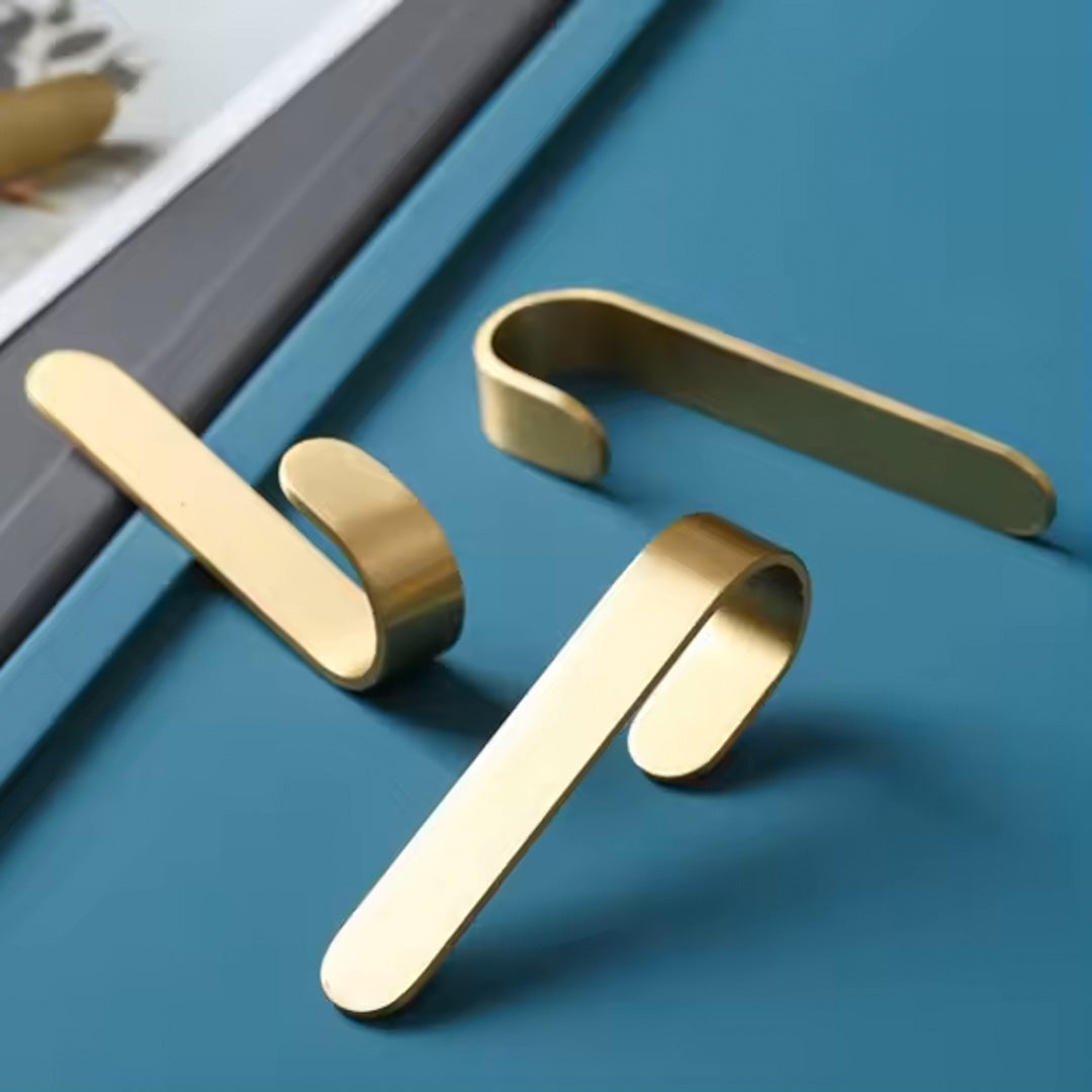 Gullfarget knagg i børstet messing festet med dobbeltsidig tape – praktisk krok til håndklær og klær.