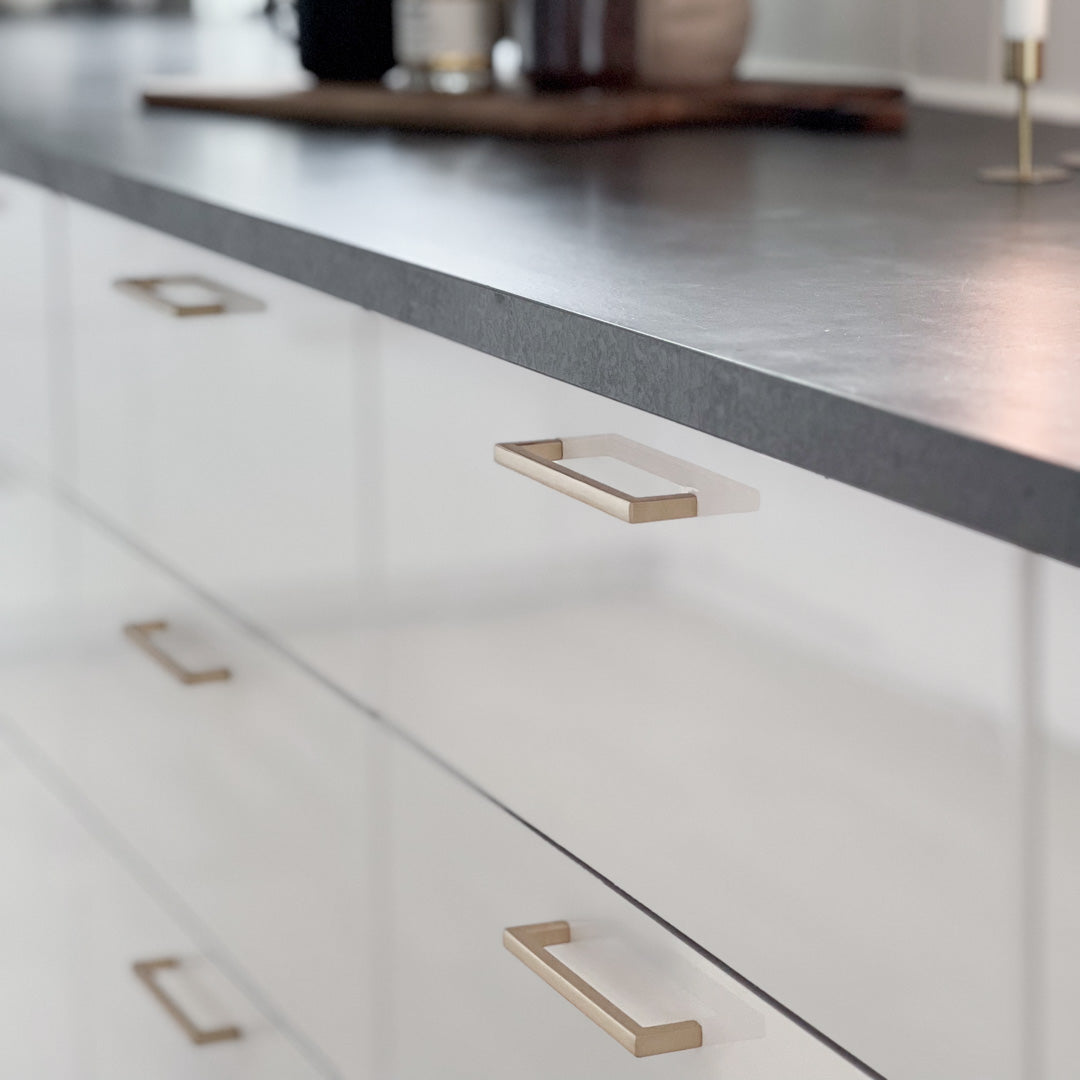 Elegant kjøkkenhåndtak i børstet messing vist i hånd for størrelsesreferanse.