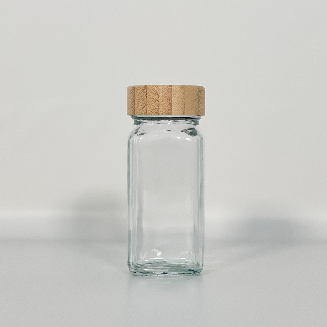 Tomt glass med bambuslokk mot hvit bakgrunn, perfekt til oppbevaring av krydder.
