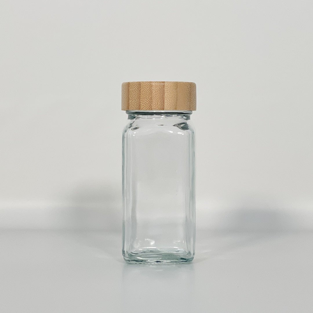 Tomt glass med bambuslokk mot hvit bakgrunn, perfekt til oppbevaring av krydder.