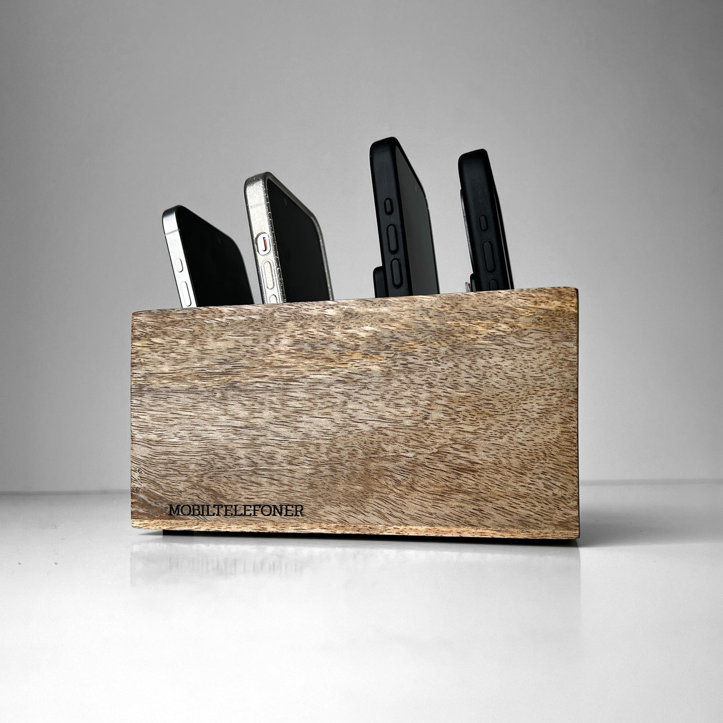 Boks til mobiltelefoner i lyst mangotre, med flere mobiler plassert i.