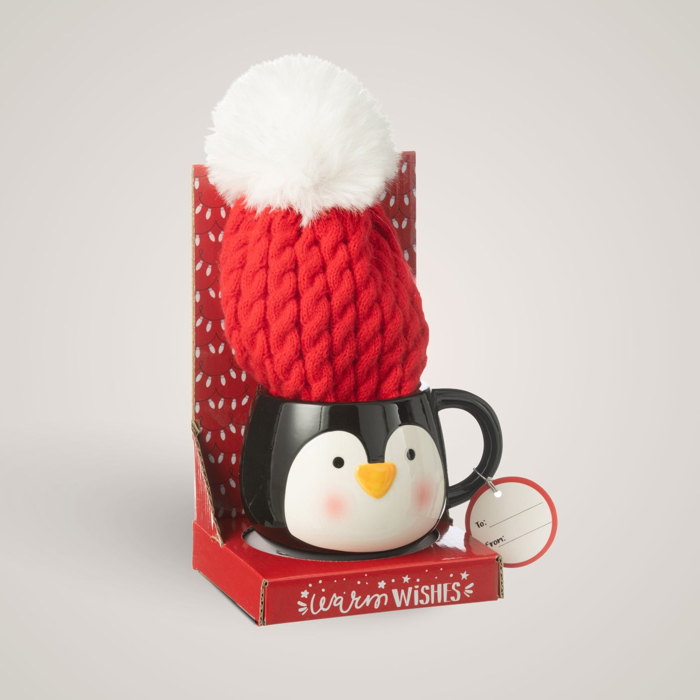 Sort pingvinkopp med rød lue og hvit dusk i gaveeske, med gaveetikett, foran lys bakgrunn.