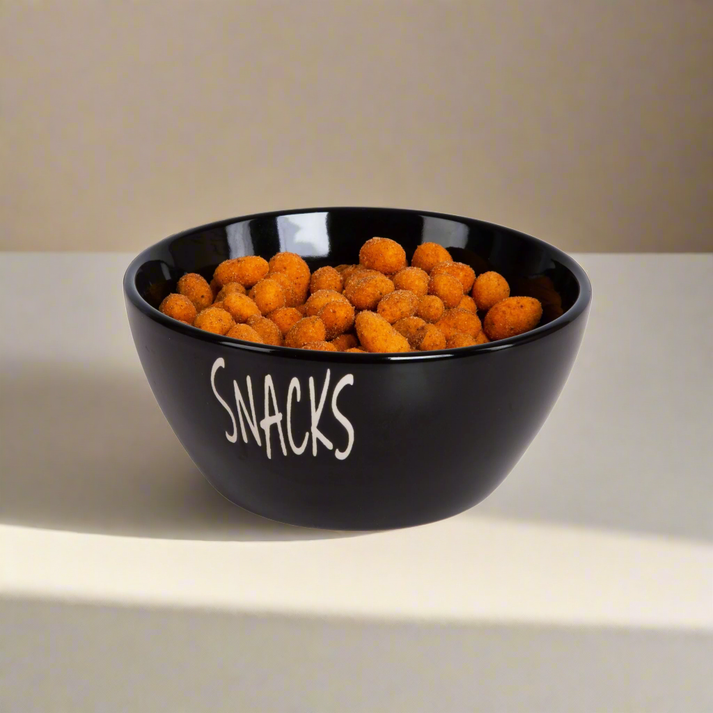 Sort snacks-skål fylt med oransje snacks, på lys overflate.