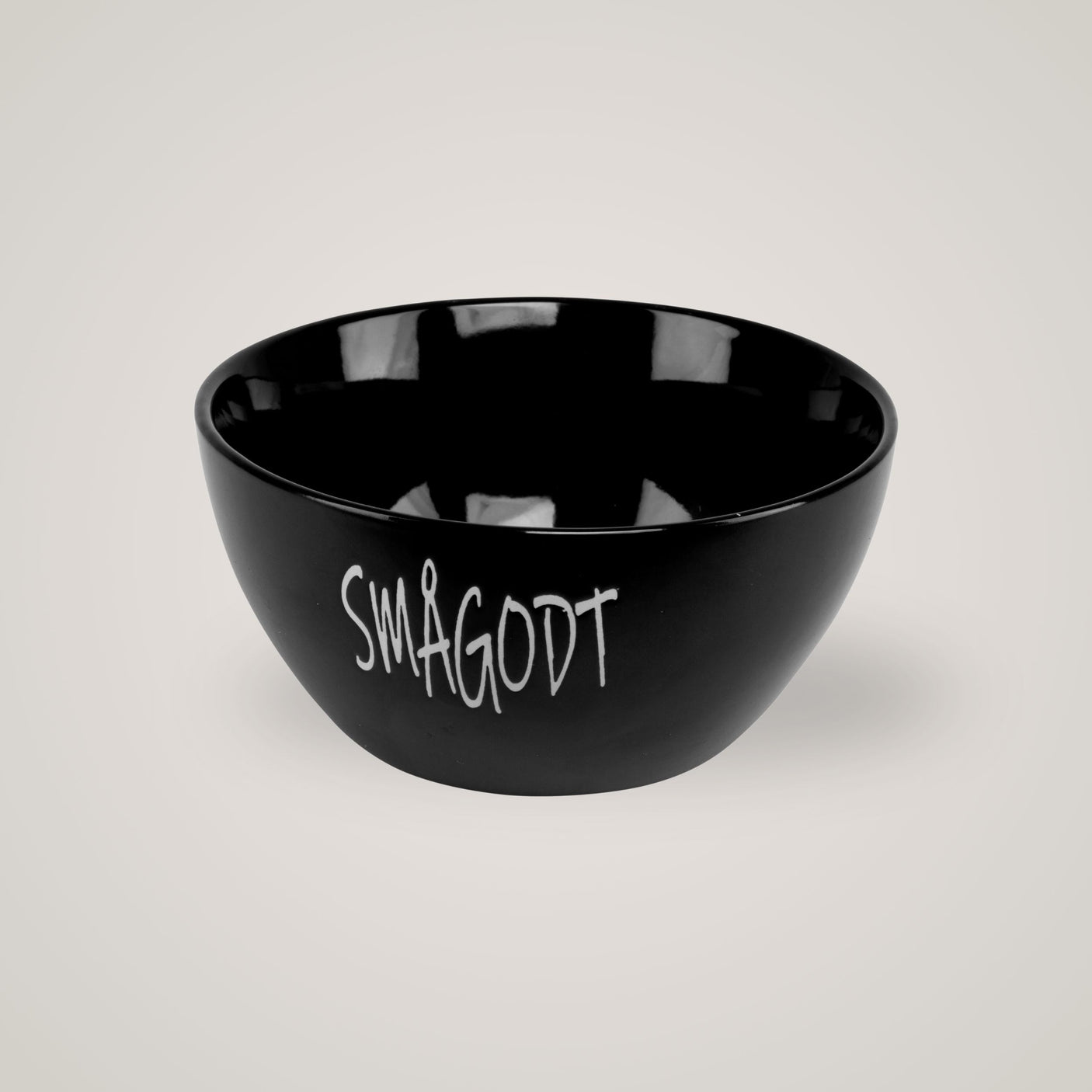 Svart skål med teksten "Smågodt", vist på beige bakgrunn med myke skygger.