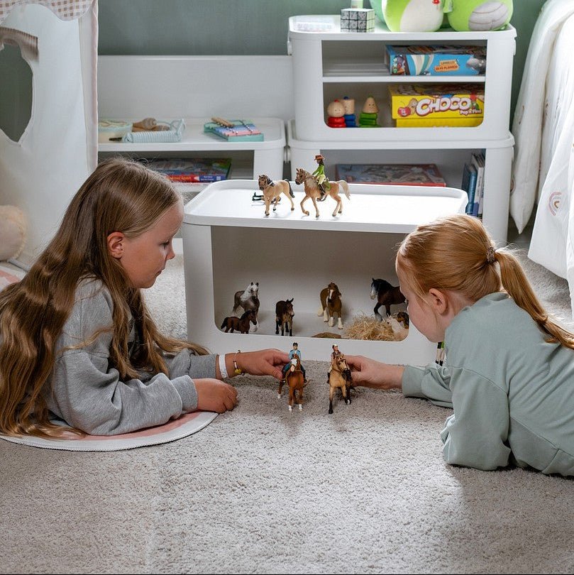 Barn som leker foran hvite oppbevaringsbokser med leker og bøker