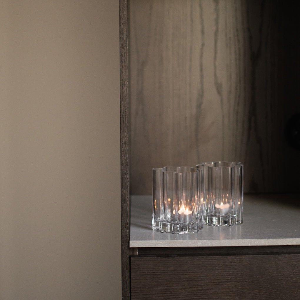 Flere klare lyslykter i rillet glass plassert på mørk hylle med elegant kontrast.