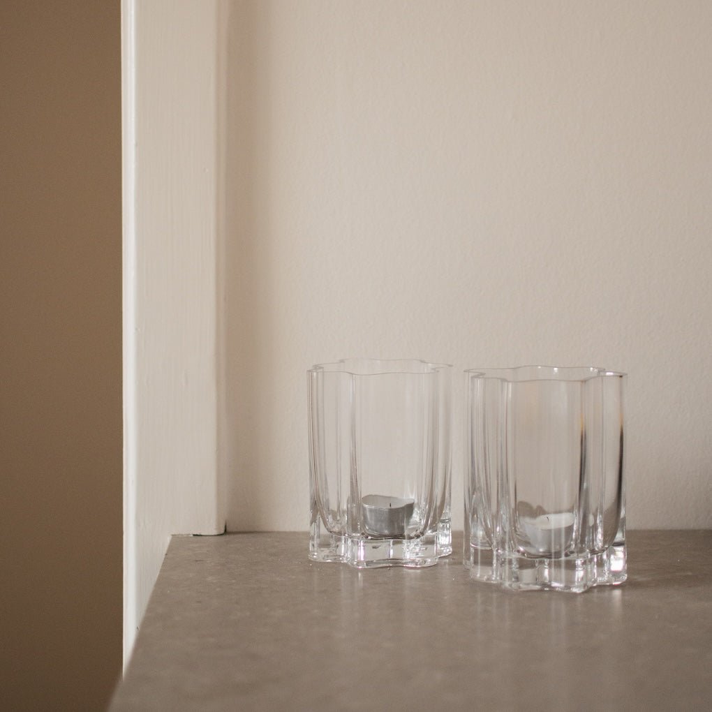 To klare lyslykter i rillet glass plassert på lys hylle i rolig og moderne interiør.