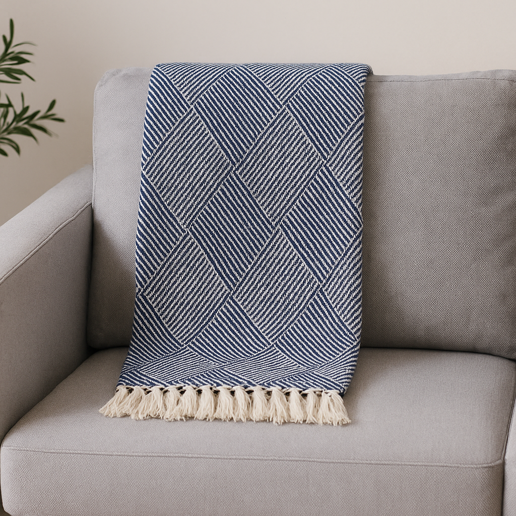 House Nordic Izmir pledd i blått og beige med frynser og geometrisk mønster – stylet over grå lenestol i moderne og lun stuekrok.