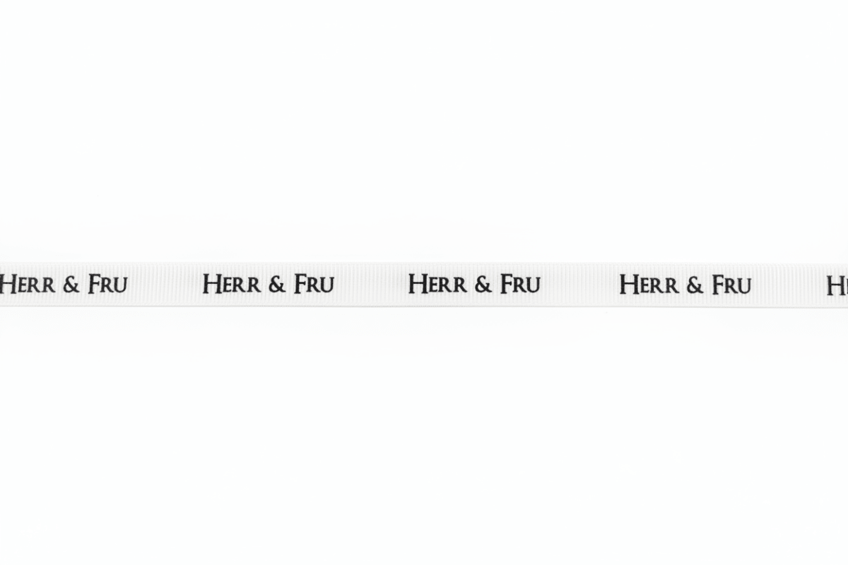 Hvitt gavebånd med repeterende sort «Herr & Fru»-tekst vist flatt og utrullet på ren lys bakgrunn - Lindas dekor