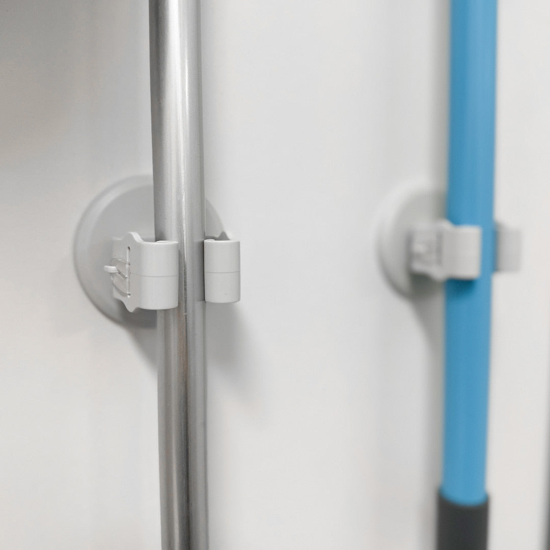 To moppeholdere montert på vegg som holder kosteskaft i metall og plast.