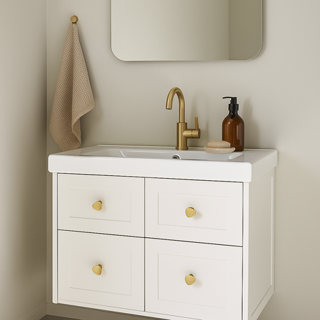 Cannes knott i børstet messing, 36 mm, på hvitt baderomsmøbel med fire skuffer og gullfarget armatur.

