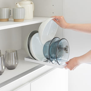 Hvit kjøkkenholder med plass til flere skåler, stående på benk ved siden av servise.