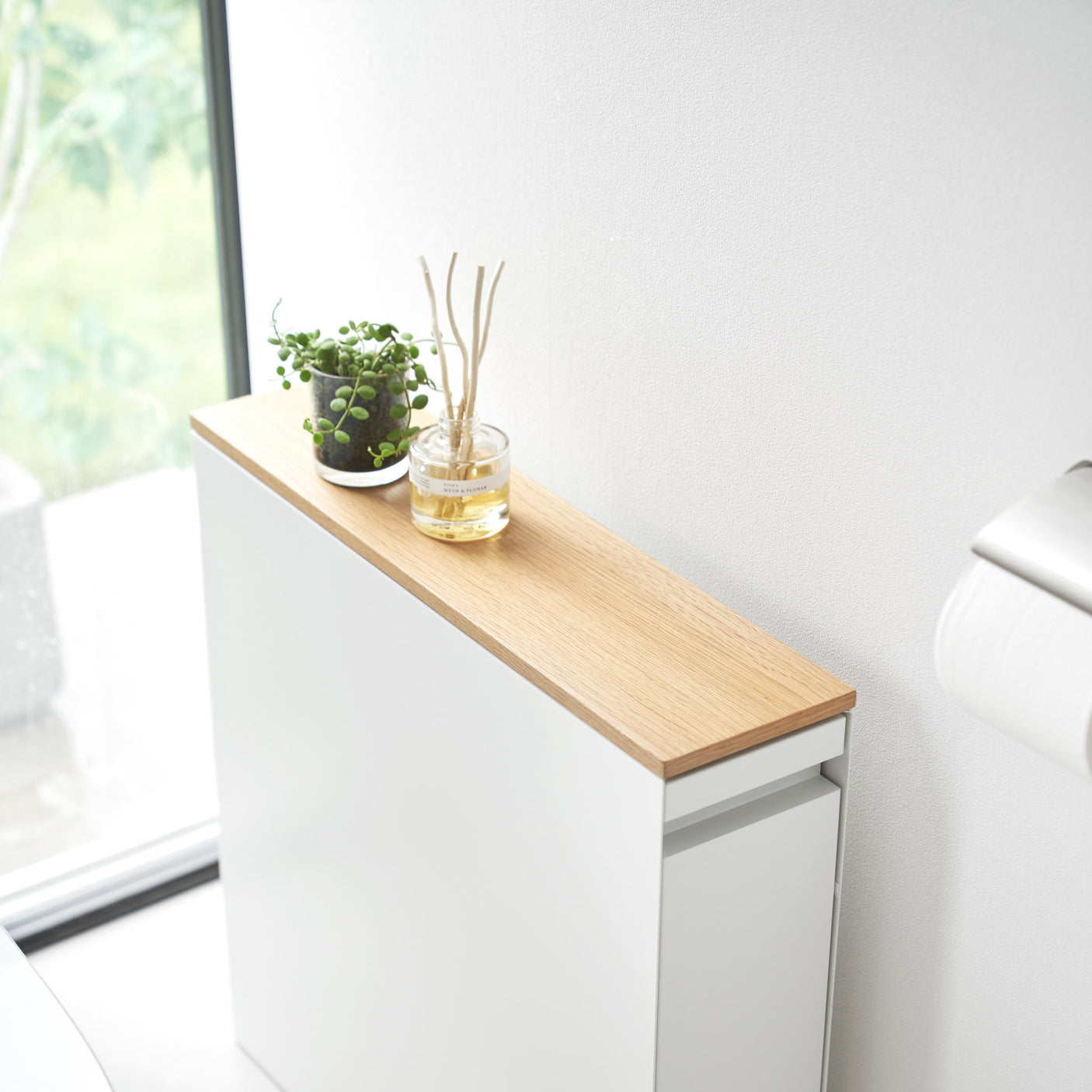 Skyvbar oppbevaringshylle i hvitt med hjul, brukt til oppbevaring av toalettruller og rengjøringsartikler.