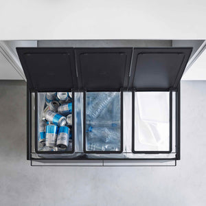 Kildesorteringsstativ med tre rom og åpne lokk som viser sortering av flasker og plast