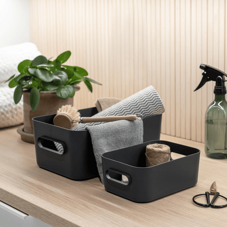 To koksgrå SmartStore Comfort oppbevaringskurver med oppvaskbørste, klut og rengjøringsutstyr på benk