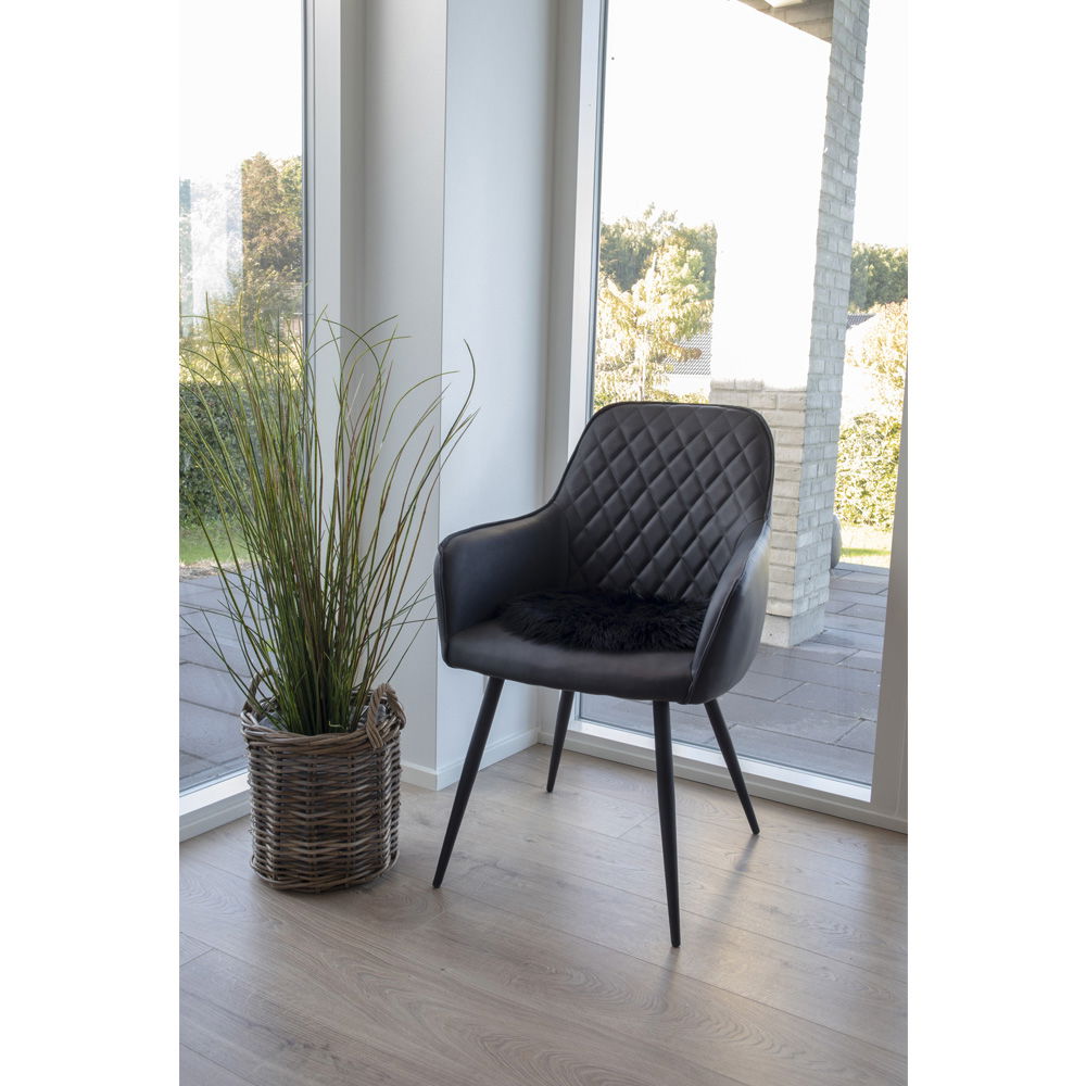 Svart sitteunderlag i kunstig saueskinn plassert på stol ved spisebord i lys stue