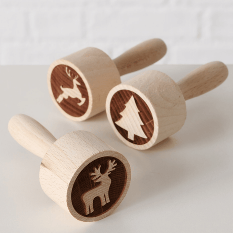 Tre kake­stempler i tre med juletre- og elgmotiv, stående og liggende på lys bakgrunn.