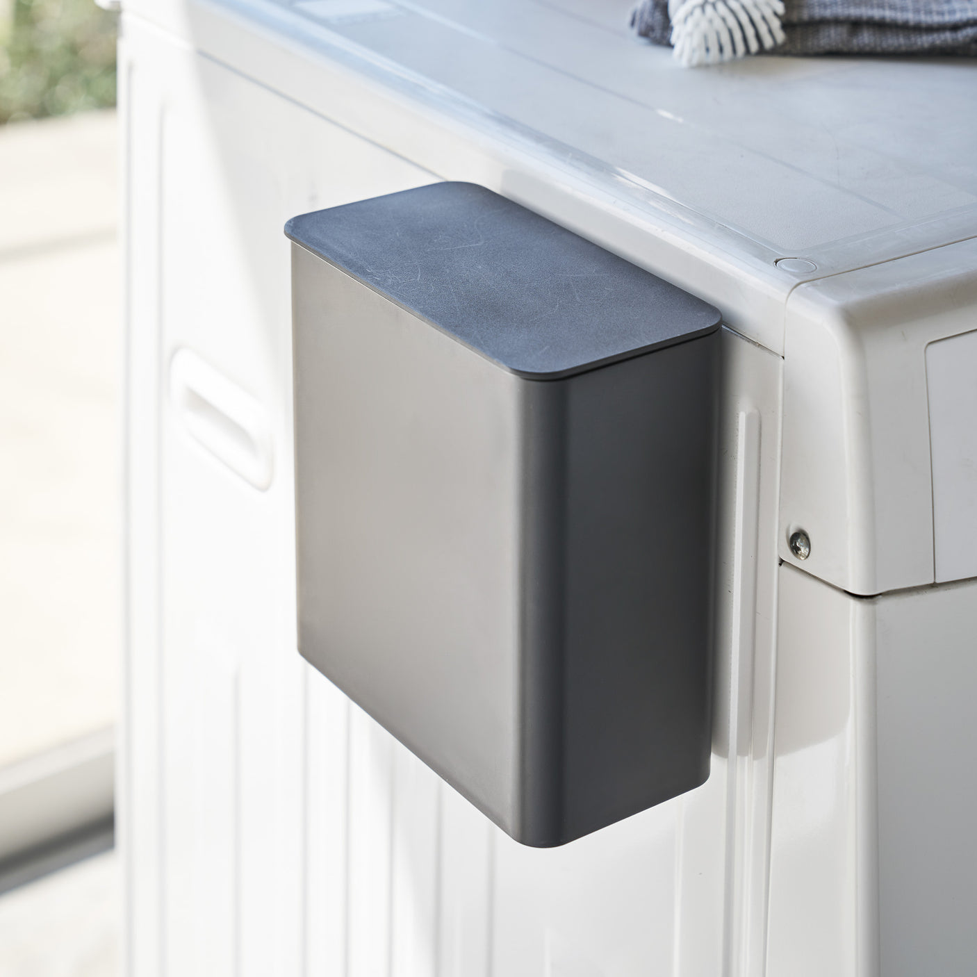 Sort magnetisk oppbevaringsboks festet på vaskemaskin.