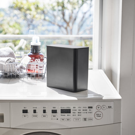 Detaljbilde av sort oppbevaringsboks på hvit maskin.