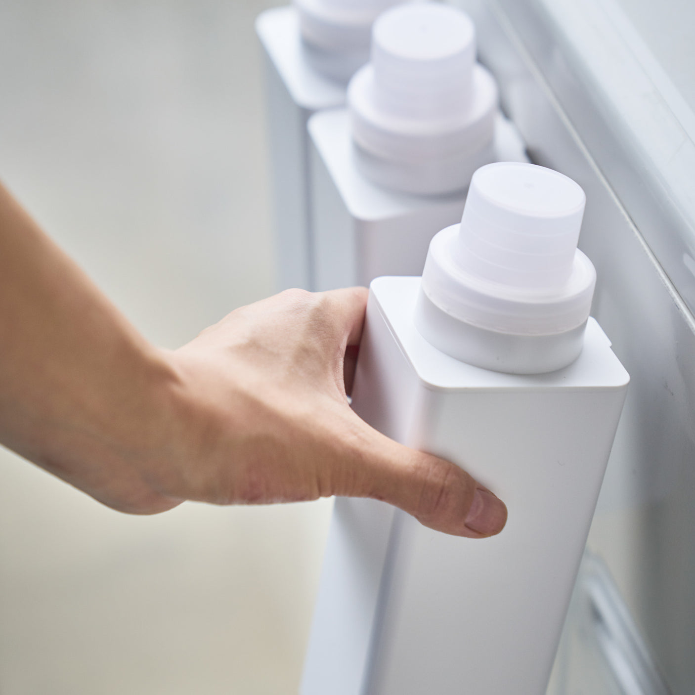 Hvit magnetisk flaske med oppvaskmiddel festet på vaskemaskin.