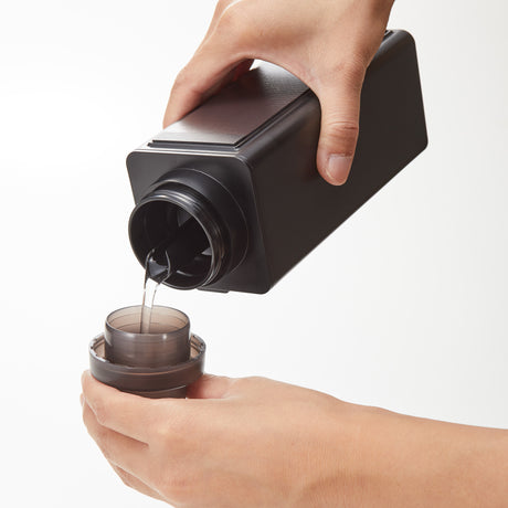 Flaske i sort plast med magnet bakside festet på vaskemaskin.